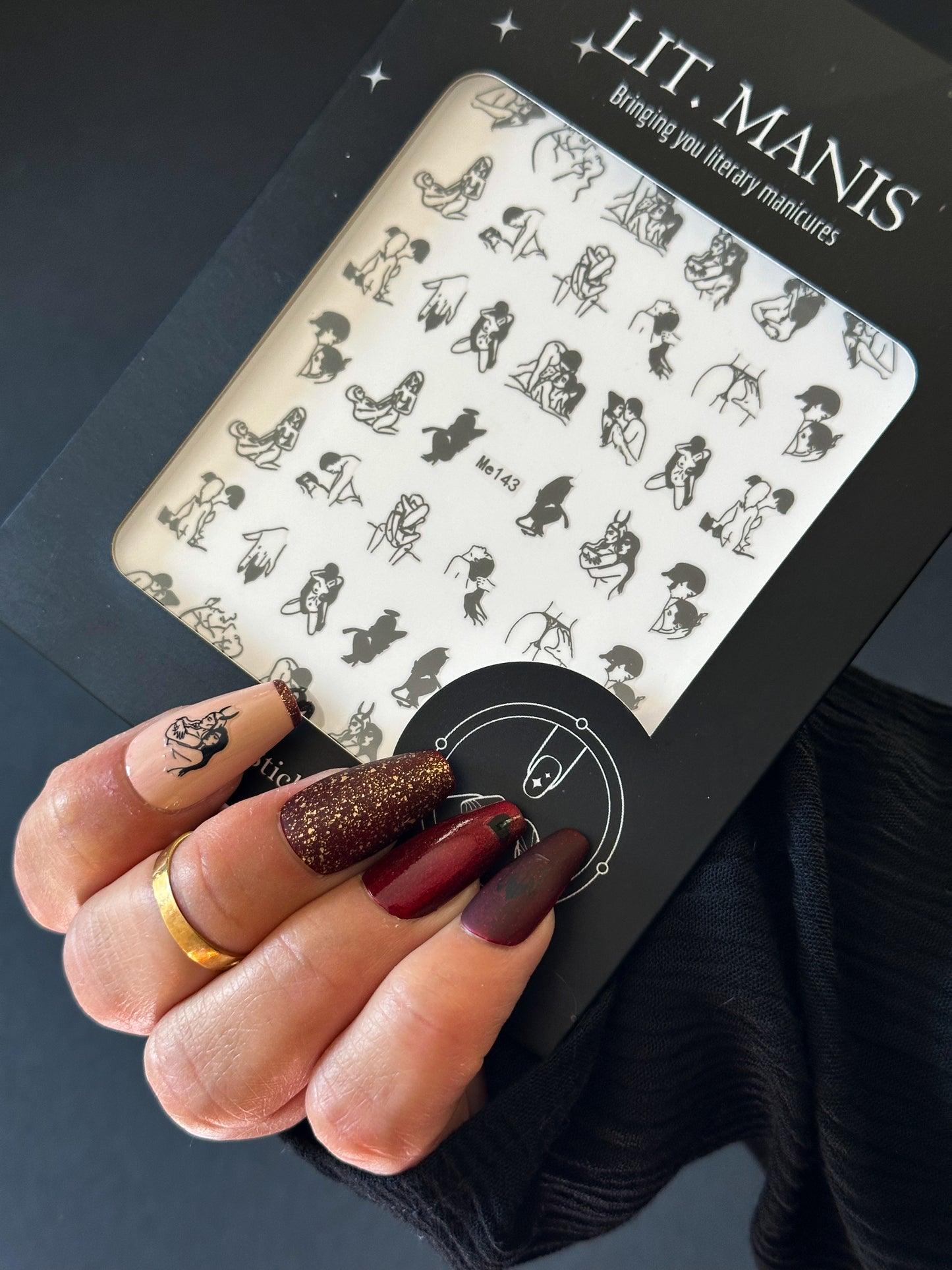 Nail art design sheet by LIT. MANIS held by a hand with painted nails.
